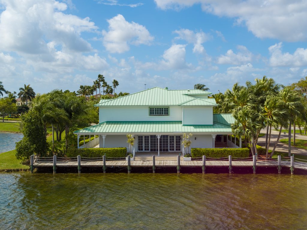 Tropical waterfront house with green roof and palm trees.