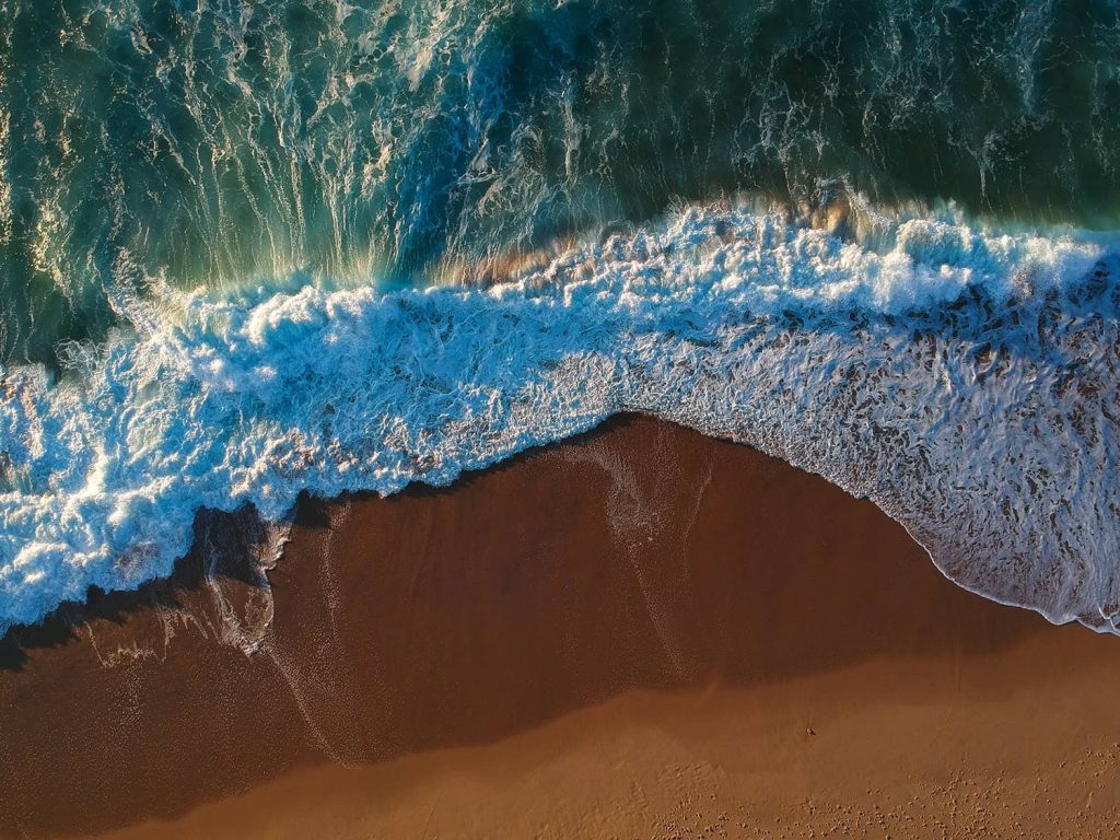 Aerial view of ocean waves crashing on sandy beach.